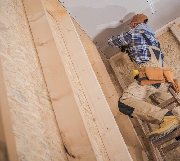 Professional Contractor Standing on Ladder During Ceiling Installation in Newly Built Residential House. Construction Theme.